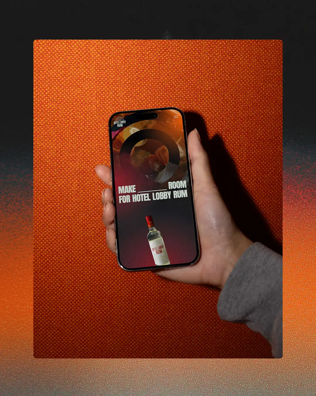 A hand holding a smartphone on a vivid orange background showing Hotel Lobby Rum branding on the screen