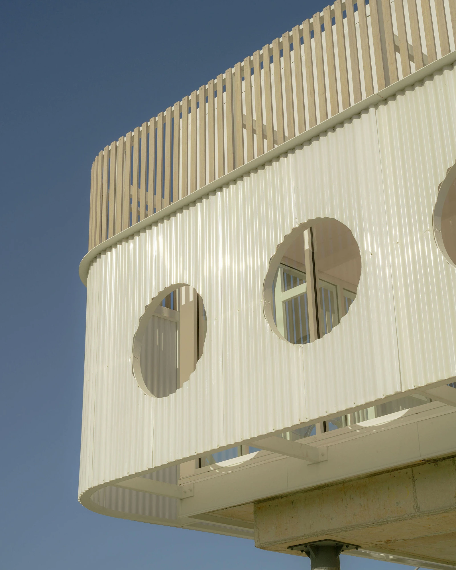 Exterior building facade with circular porthole-style windows on a white cream surface photographed from below
