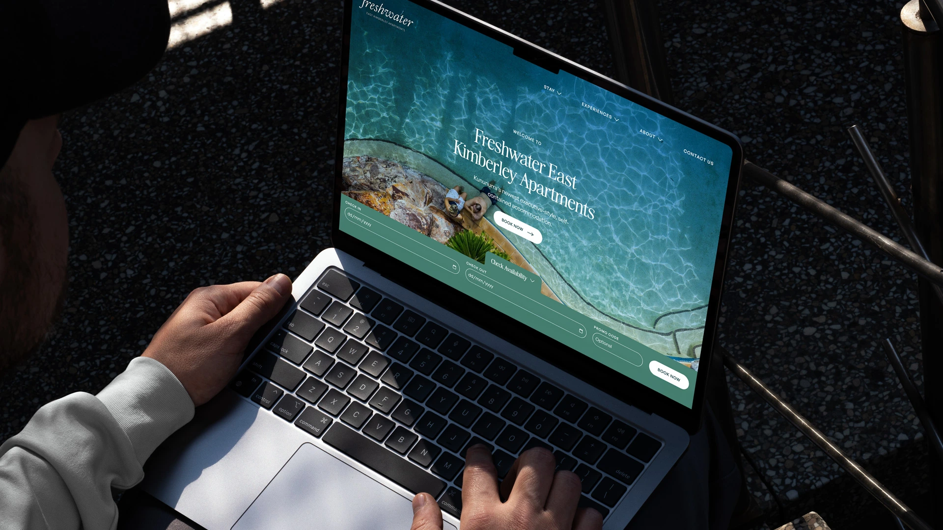 The Freshwater venue website displayed on a MacBook on a wooden surface showing coastal ocean photography