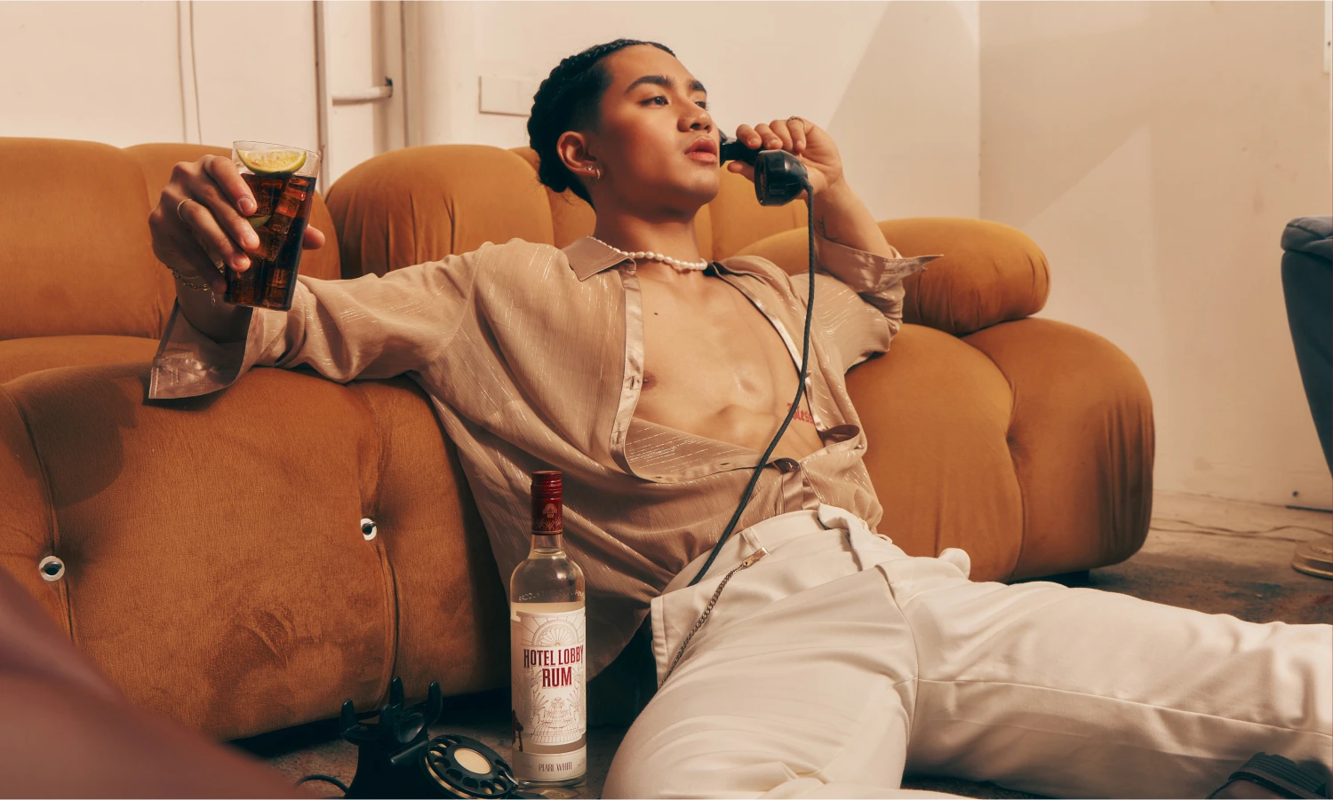 Person in a camel-coloured outfit lounging in an orange room holding a cocktail — Hotel Lobby Rum