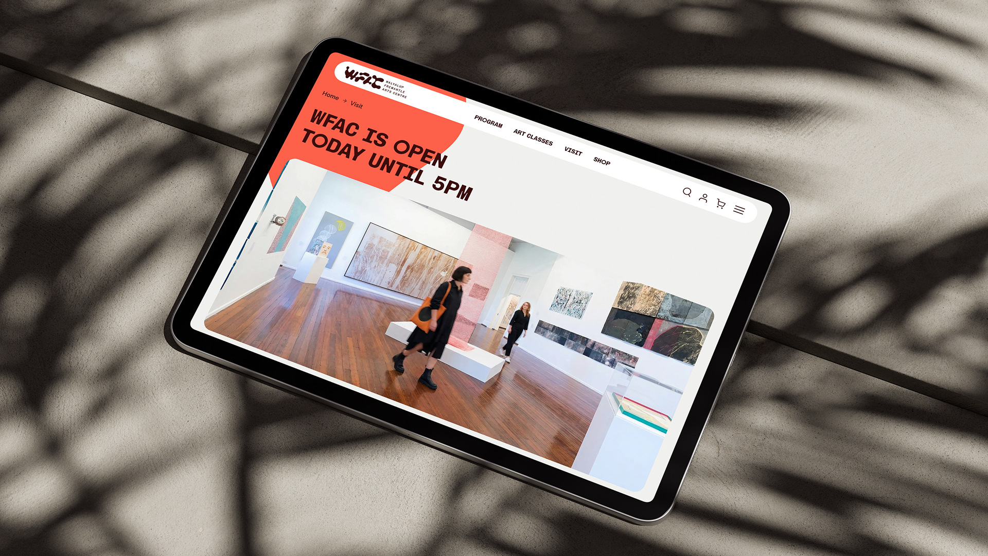 iPad mockup on a wooden surface with palm leaf shadows, showing a website design